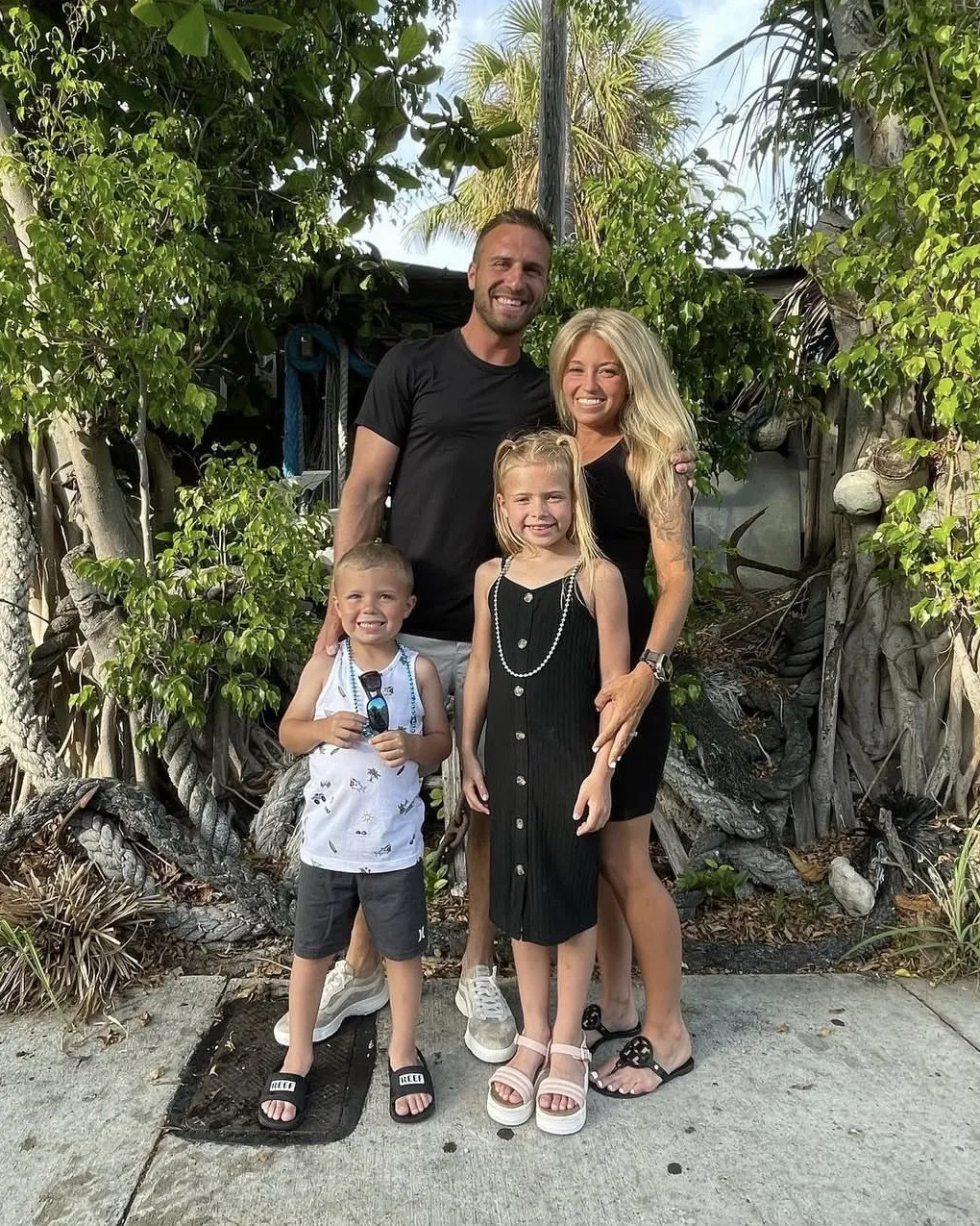 Mike and Kelsey Coppa with their kids, Kinsley and Carter, standing on a sidewalk under banyan trees and palms