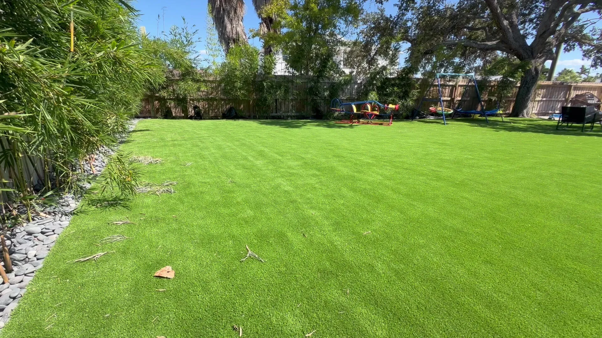 A large artificial turf play yard with a swing set and a teeter-totter along the back fence