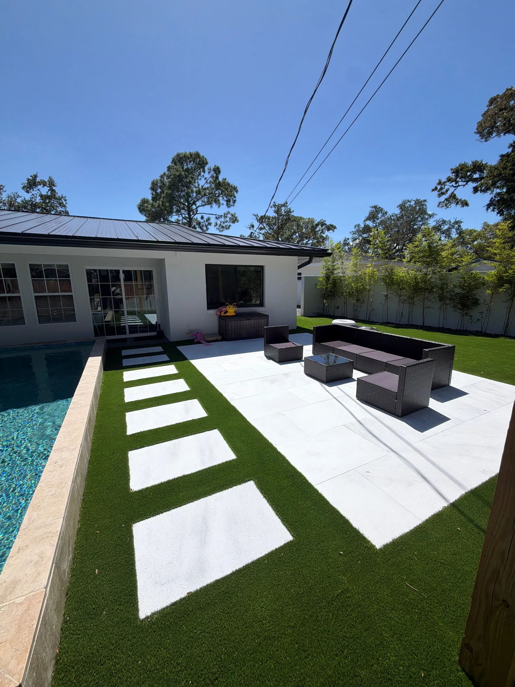 Turf strips between paver steppers on a pool deck, looking back toward the house