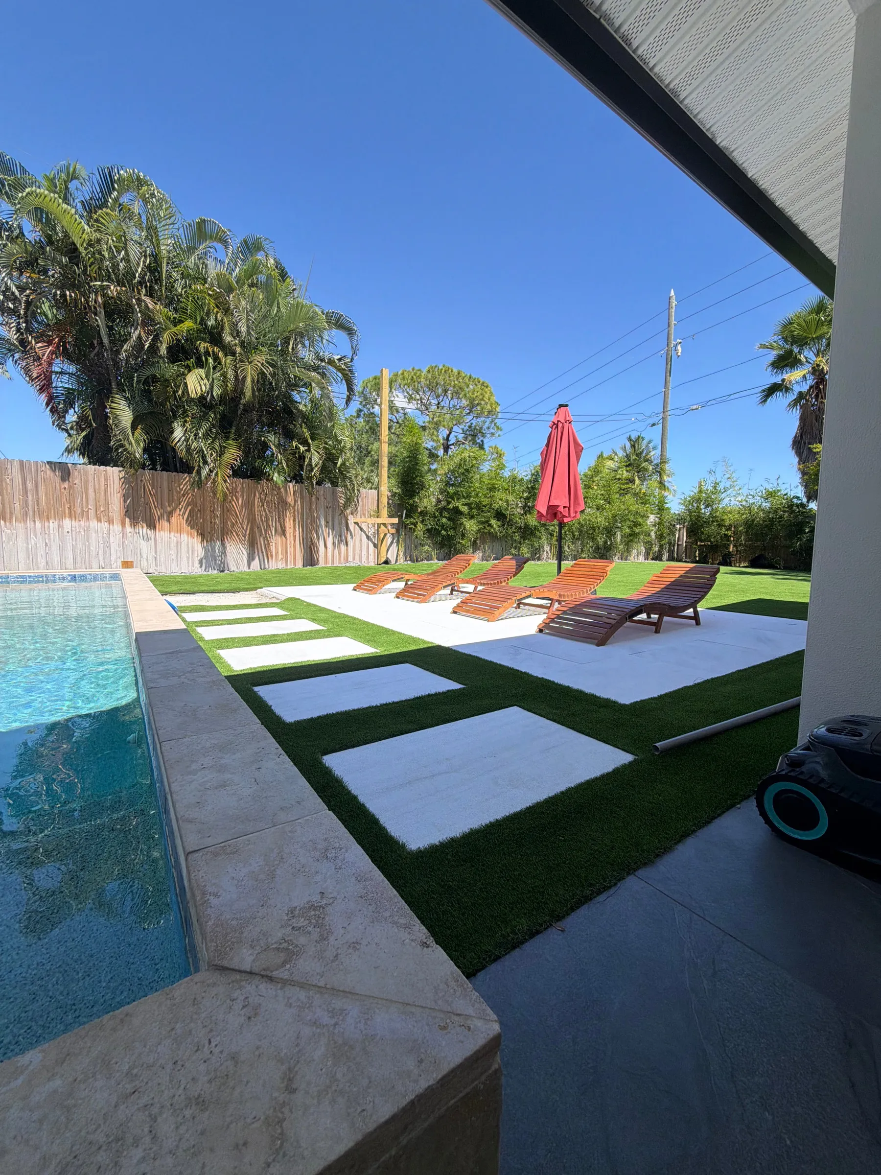 Turf pool deck with paver steppers and lounge chairs under a red umbrella