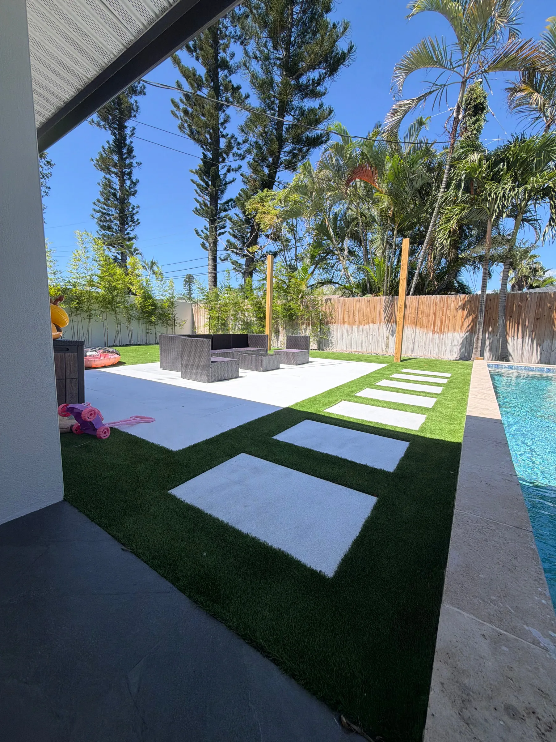 Pool deck with turf strips between white pavers
